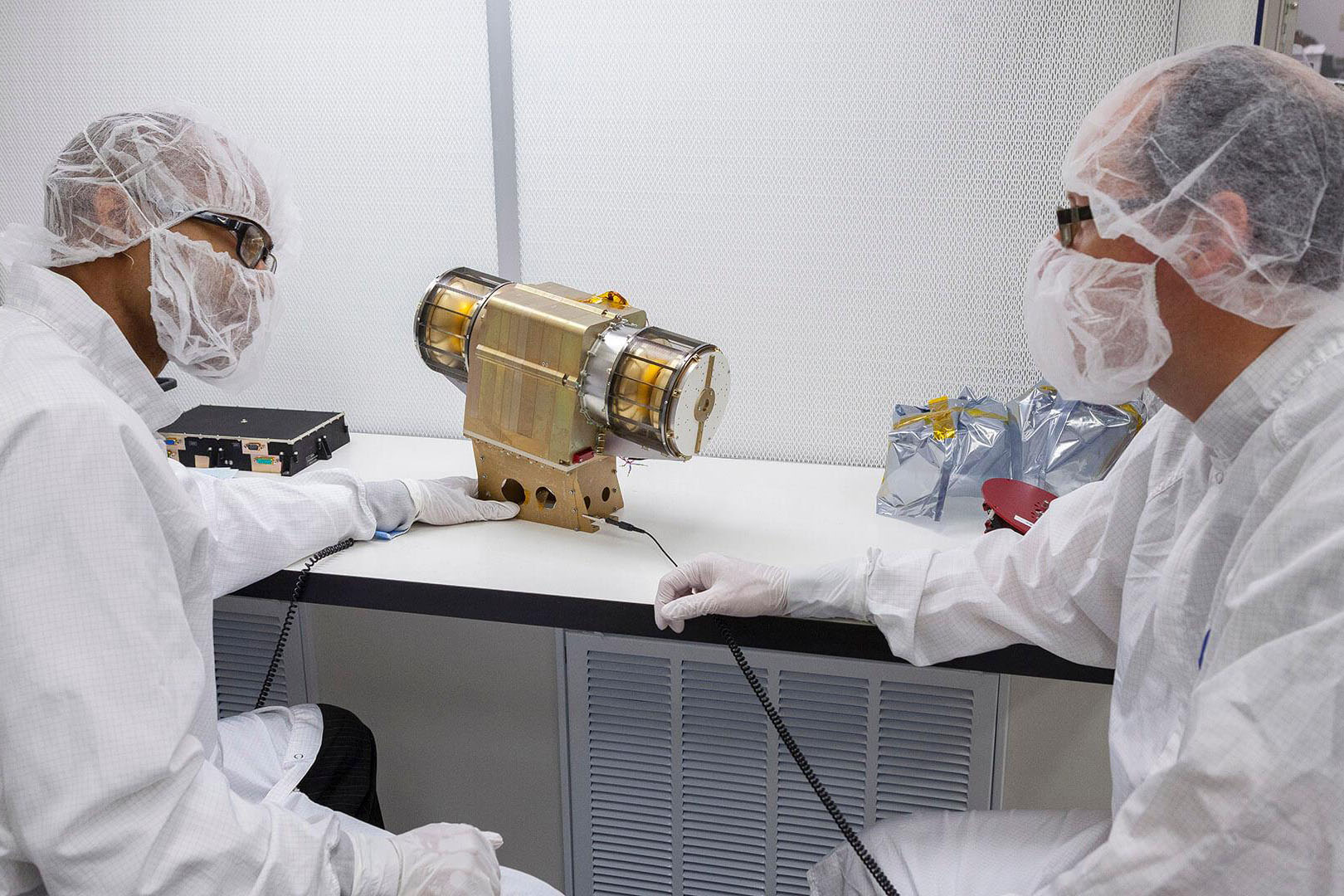 Two scientists in white lab coats observing a metallic gold space instrument
