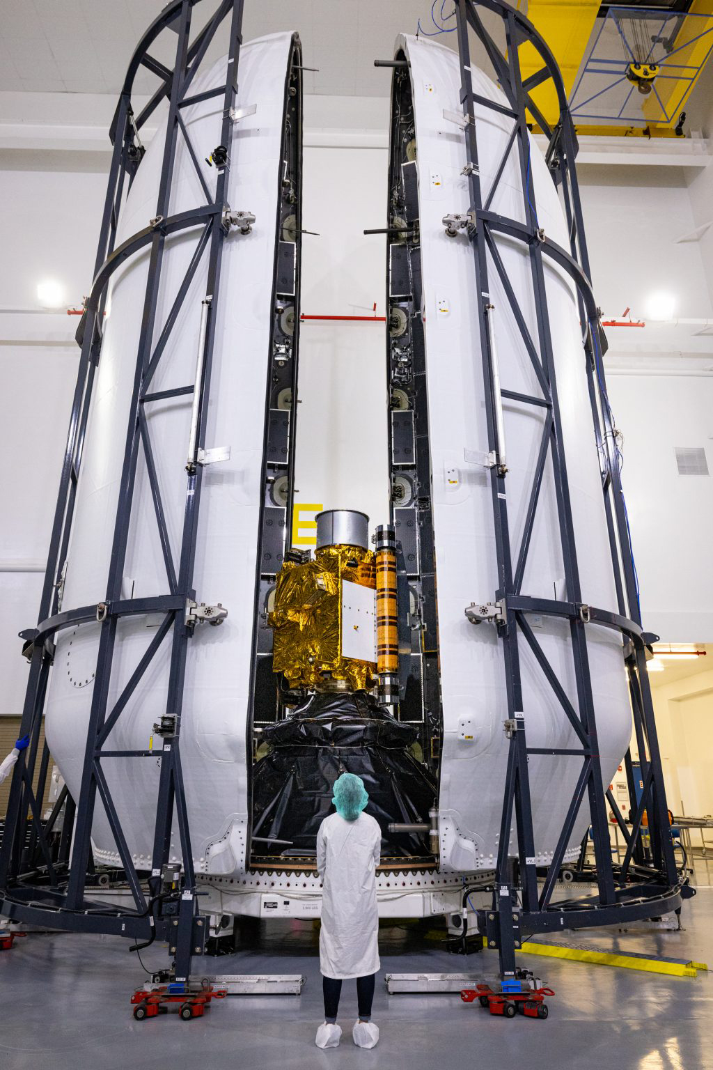 A person dressed in PPE looks on at the DART spacecraft inside the payload fairing