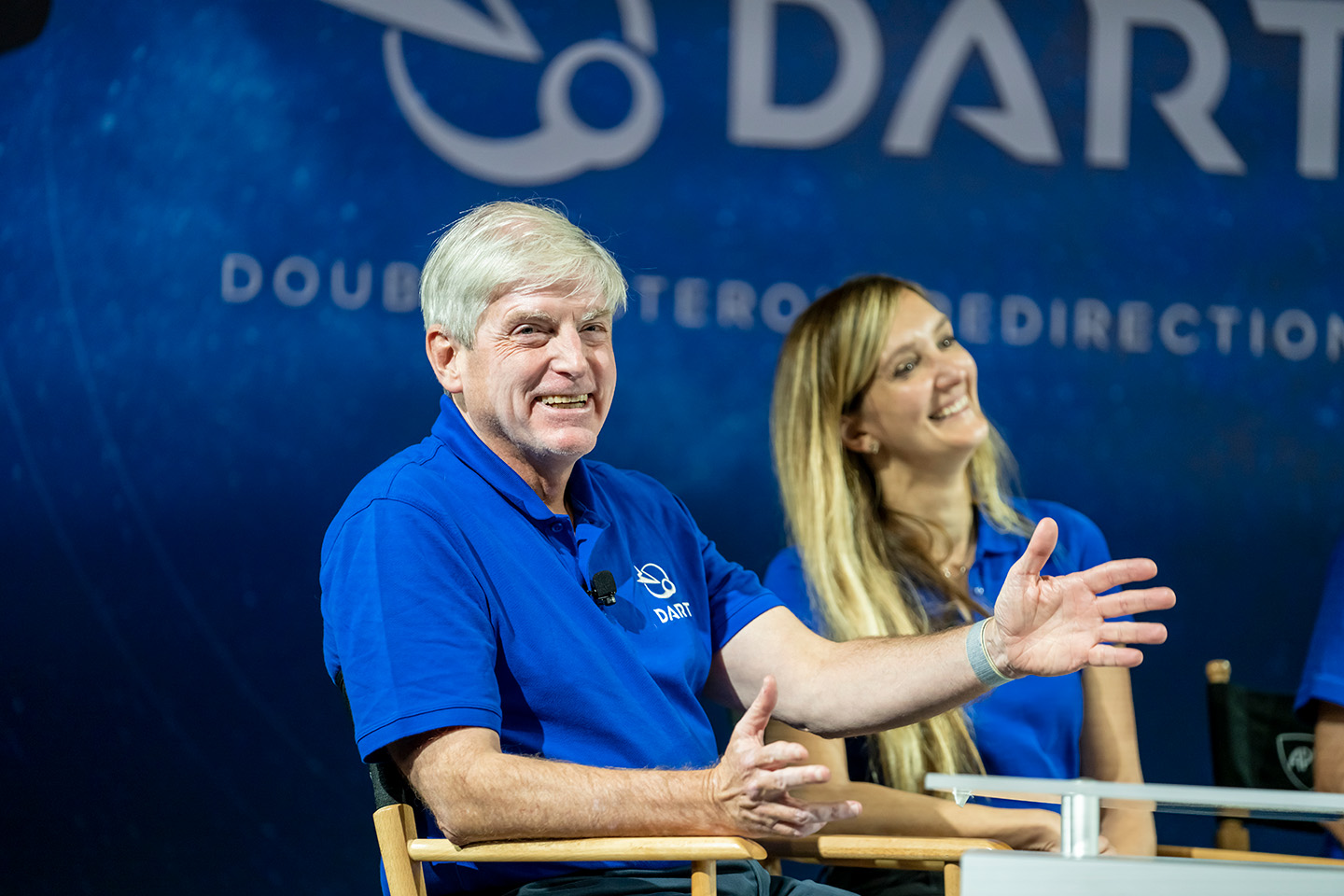 Ed Reynolds sits in a chair next to Elena Adams with the DART logo on a board behind them