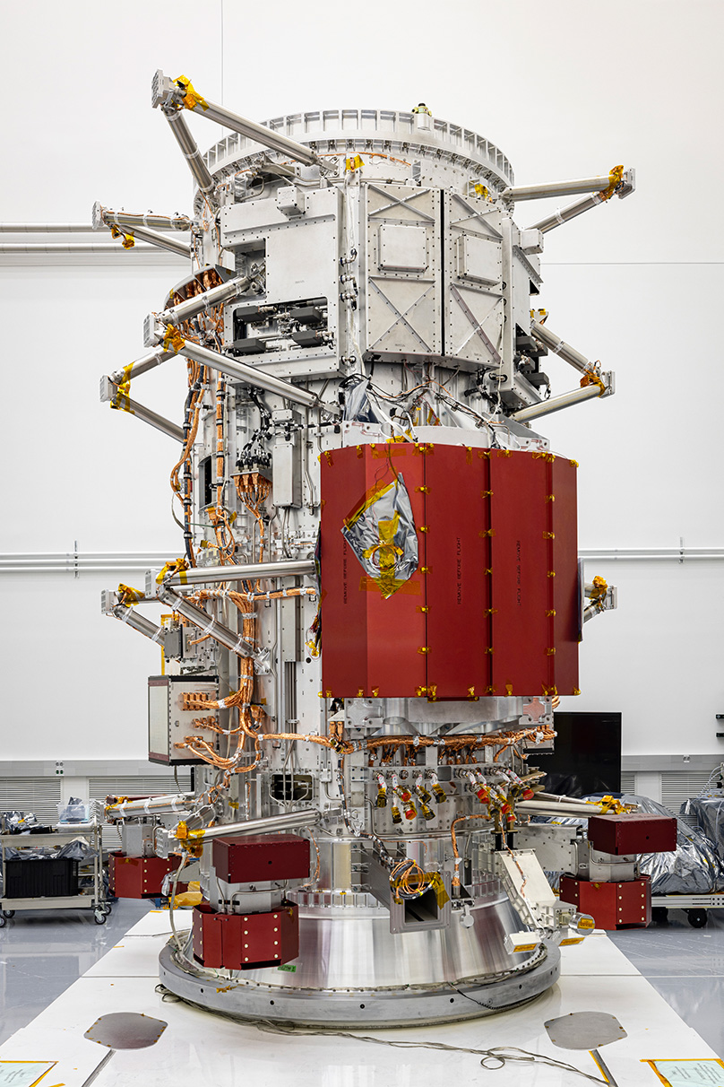 An image of the Europa Clipper propulsion module, with several metal arms jutting from its sides and the RF module in red