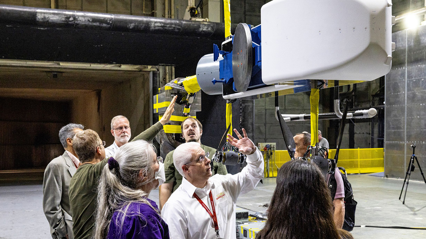 A group of people look up and examine a model of the Dragonfly rotorcraft lander after it went through wind tunnel tests