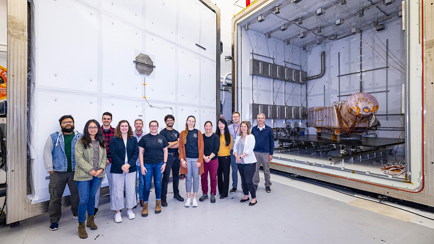 Members of the Dragonfly team stand outside the giant box-like Titan Chamber, where a model of the Dragonfly spacecraft sits