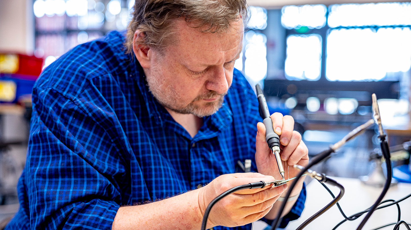 A photo of Rob Barnes working with a soldering iron on an electronics chip
