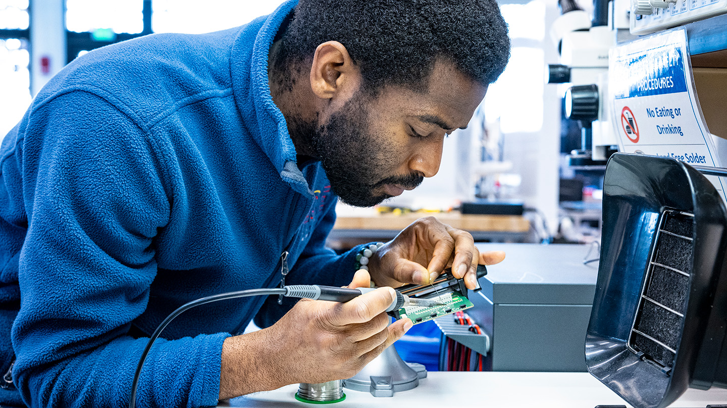 A photo of Adebayo Eisape working with a soldering iron on an electronics chip