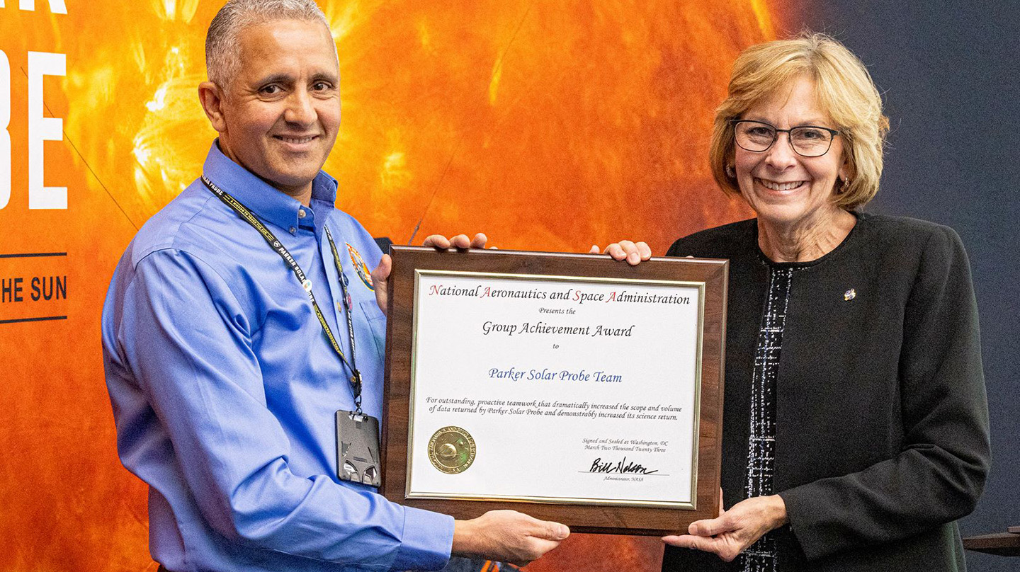 A photo of Nour Raouafi with NASA's Peg Luce, both holding a group achievement award. A Parker Solar Probe poster hangs behind them.