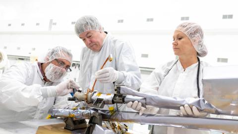 Engineers working with an instrument while wearing white, clean-room protective clothing