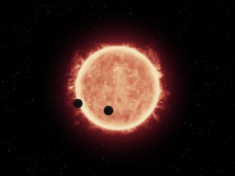 Silhouettes of two planets as they orbit a fiery star 