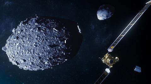 A spacecraft covered in gold foil and a tiny box-like companion satellite are in a space scene, with two asteroids: one gray, ellipsoidal and covered in the rocks, the other more pyramid-like; both are gray 