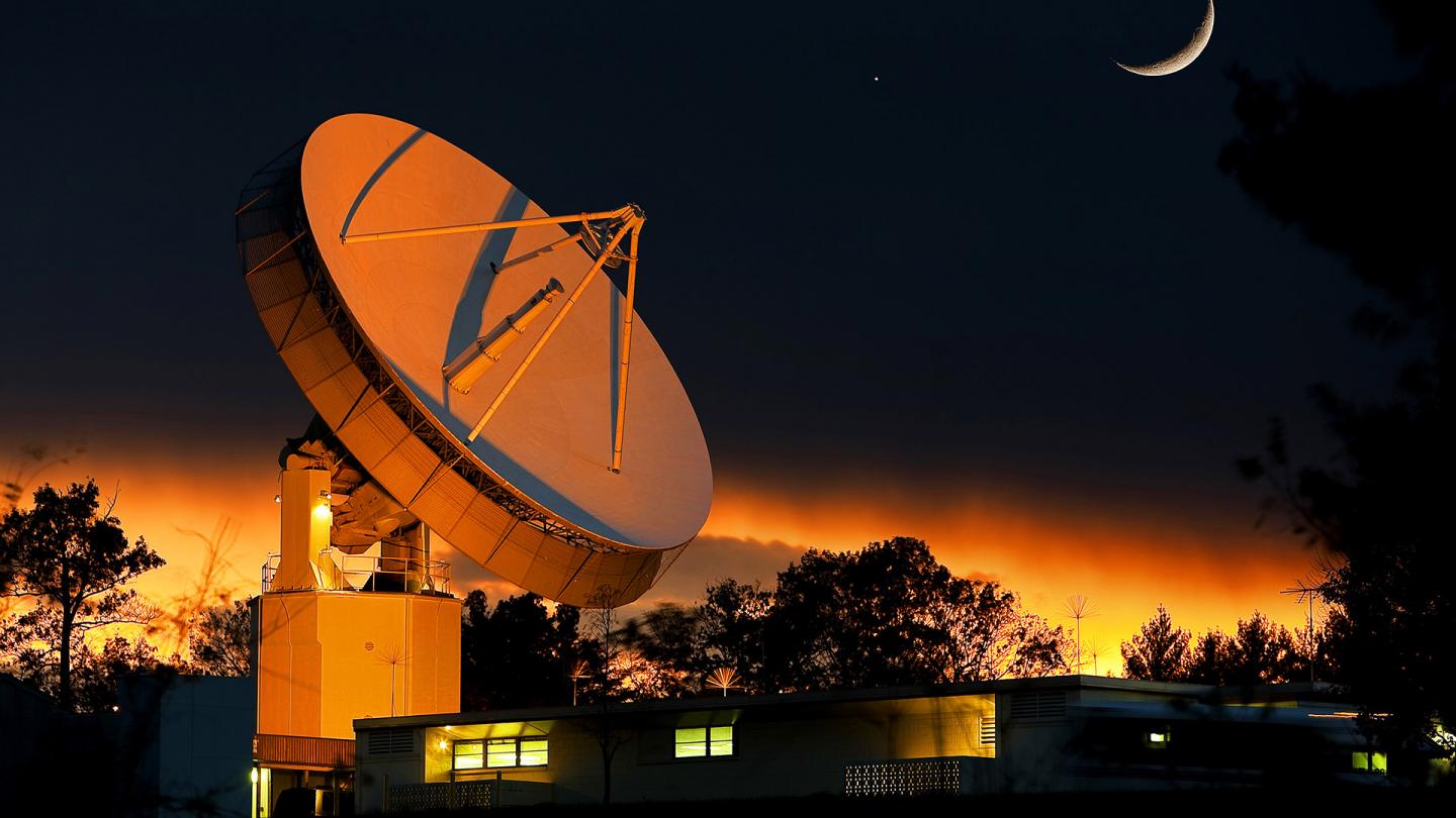 APL&#039;s large satellite dish aglow in orange light under the moon
